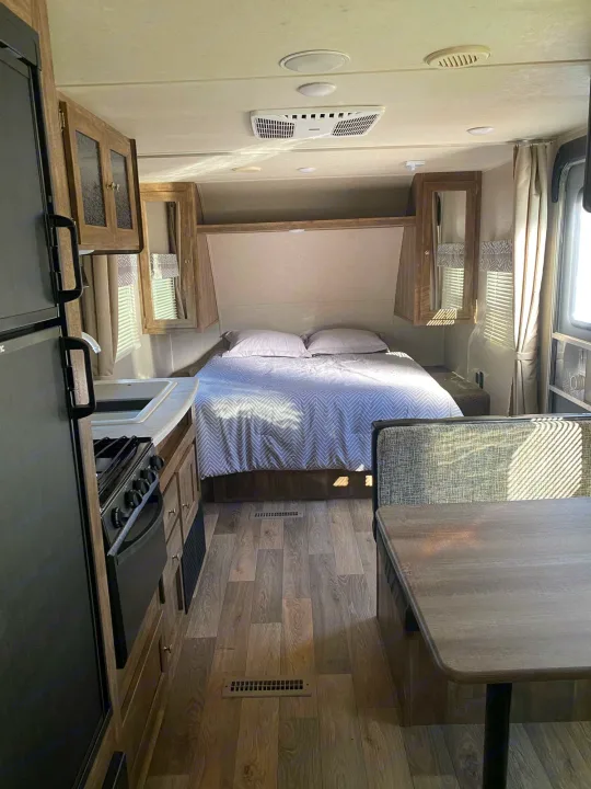 Inside a cozy RV rental: bedroom with patterned bedding, compact kitchen, and dinette. Functional travel space.. Forest River Puma 2019