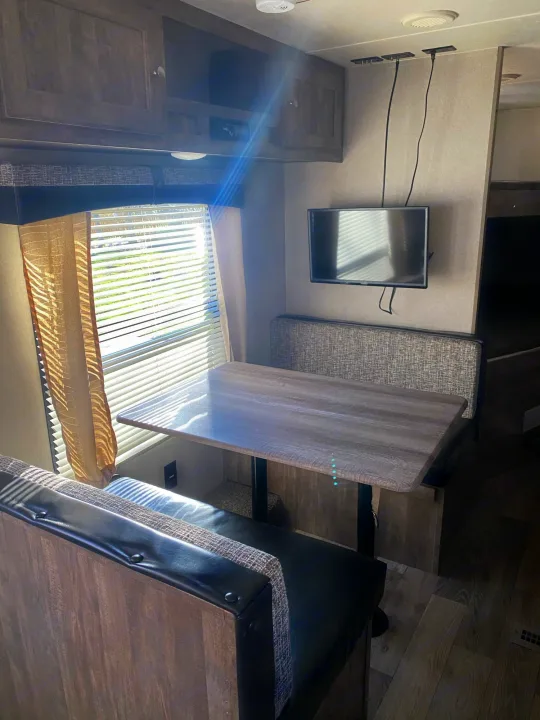 An RV rental's dinette area features a wooden table, two upholstered benches, and a wall-mounted TV.. Forest River Puma 2019