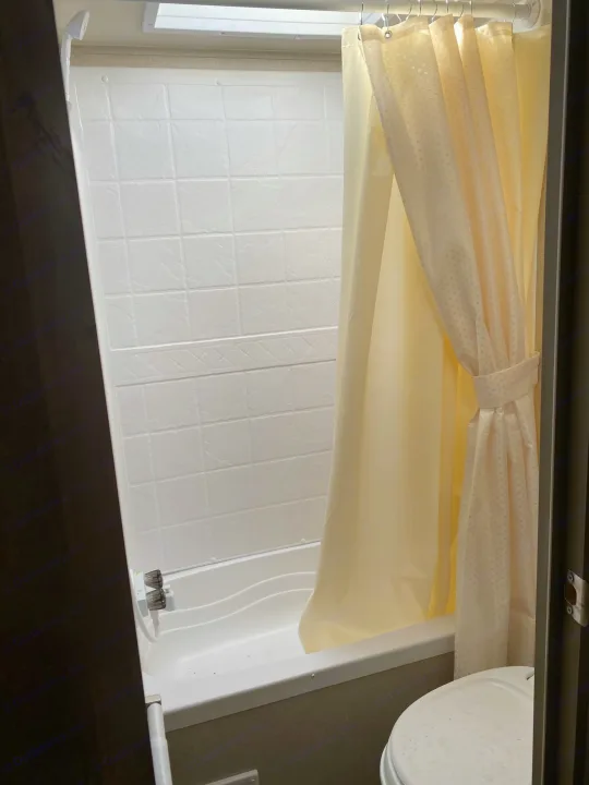 This compact shower and bathtub combo is part of an RV rental bathroom, featuring white walls and a cream curtain.. Forest River Puma 2019
