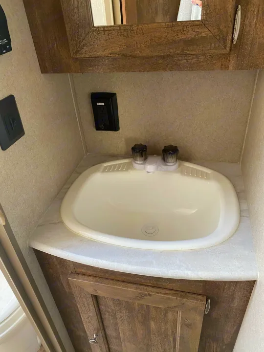 Inside an RV rental: a compact bathroom vanity with a white sink, faucet, wood cabinet, and electrical outlets.. Forest River Puma 2019