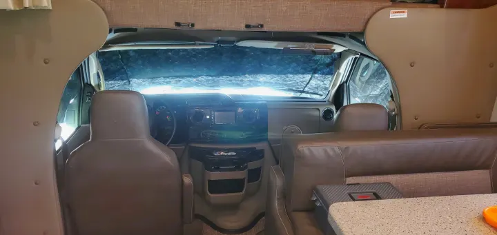 RV rental interior: The front cab area with dashboard, steering wheel, seats, and covered windshield, from the living space.. Holiday Rambler Vesta 2017
