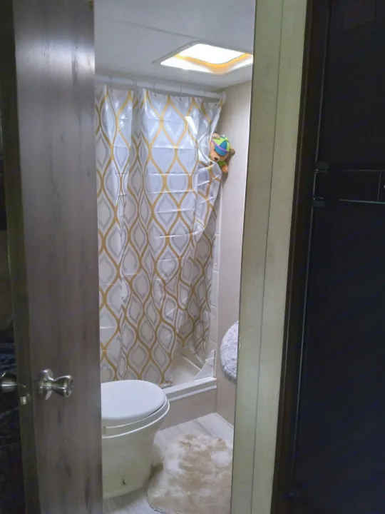 RV rental bathroom with white toilet, gold & gray patterned shower curtain, overhead skylight, and a plush toy peeking.. KZ Other 2017