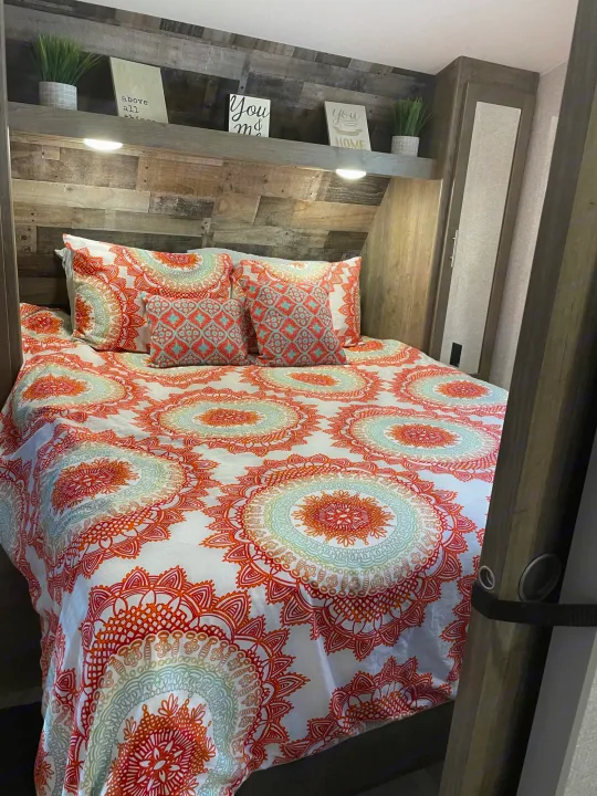 Cozy RV rental bedroom featuring a bed with vibrant mandala bedding, wooden headboard, and decorative shelf. Perfect for travelers.. Dutchmen Aspen Trail 2021