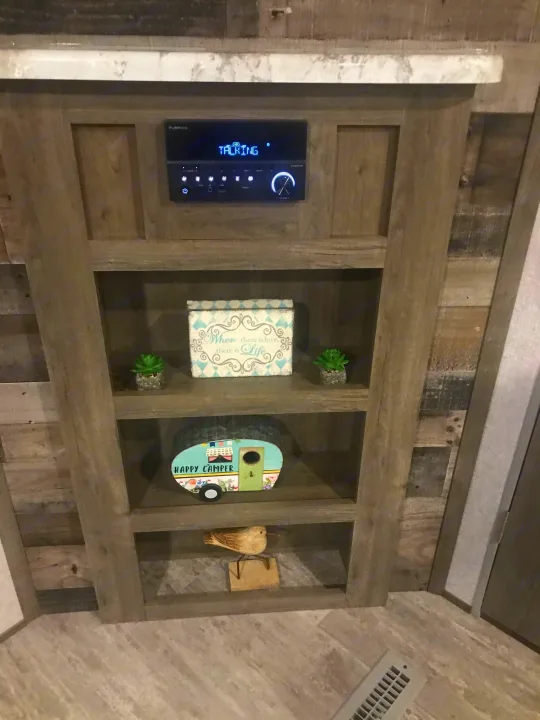 Inside an RV rental: built-in wooden shelves display a Furrion stereo, "Happy Camper" decor, and succulents.. Dutchmen Aspen Trail 2021