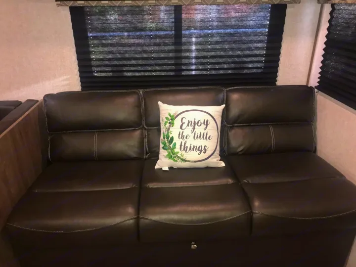 Relax in this cozy RV rental's dark leather sofa with a decorative pillow, set against window blinds.. Dutchmen Aspen Trail 2021
