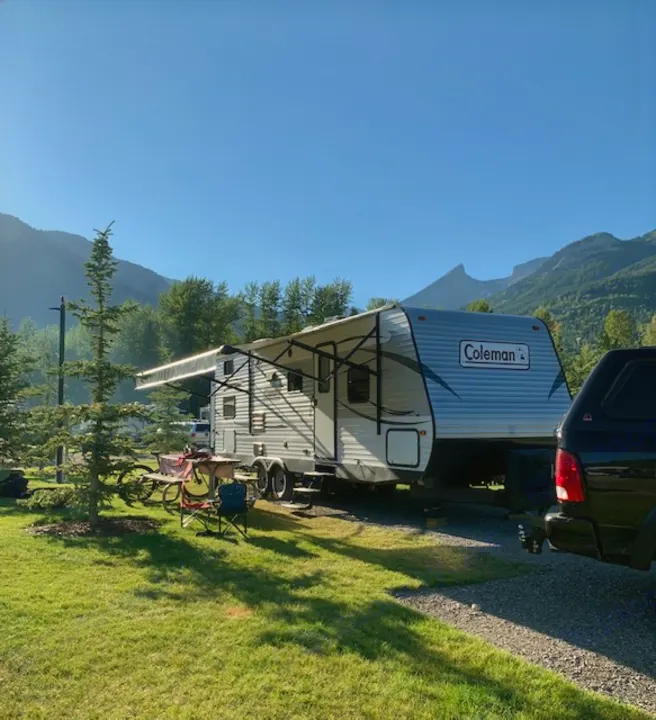 This image shows a Coleman RV rental parked at a scenic mountain campsite with a truck, picnic table, and chairs.. Coleman Lantern Edition 262 BH 2017