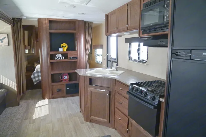An inviting RV rental interior showcasing a compact kitchen, built-in entertainment, and a curtained bedroom area.. Coleman Lantern Edition 262 BH 2017