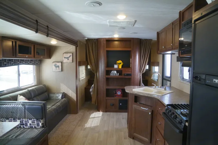 This RV rental showcases a spacious interior with a kitchen, living area, and dining space. Dark wood cabinets complement modern furnishings.. Coleman Lantern Edition 262 BH 2017