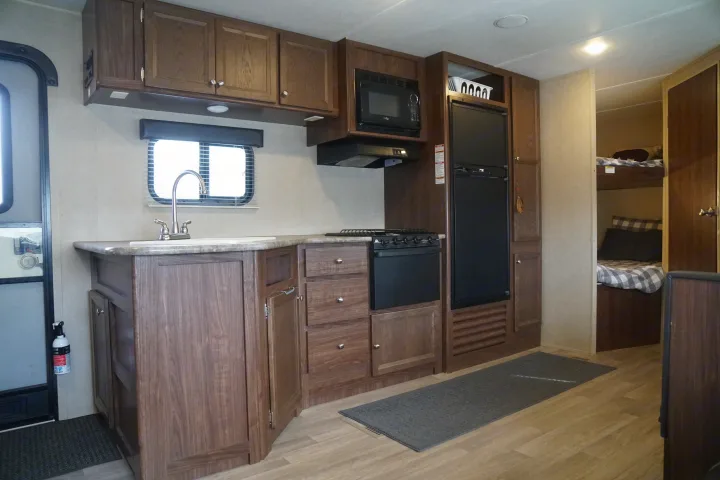 Inside this RV rental: functional kitchen with sink, stove, microwave, fridge, and cozy bunk beds visible.. Coleman Lantern Edition 262 BH 2017