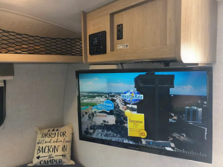 An RV rental's cozy interior features a Furrion TV displaying weather, an RV tech control panel, and net storage.. Forest River Rockwood Geo Pro 2021
