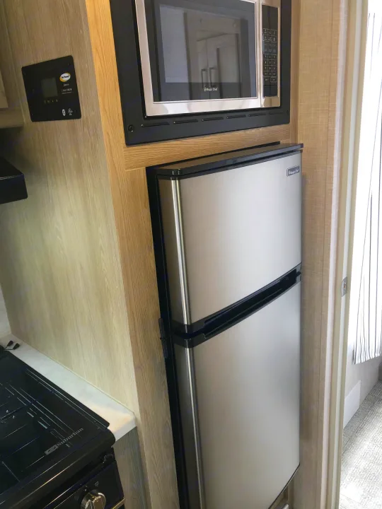 Typical rv rental kitchen with stainless microwave, dual refrigerator, control panel, and stovetop, ready for use.. Forest River Rockwood Geo Pro 2021