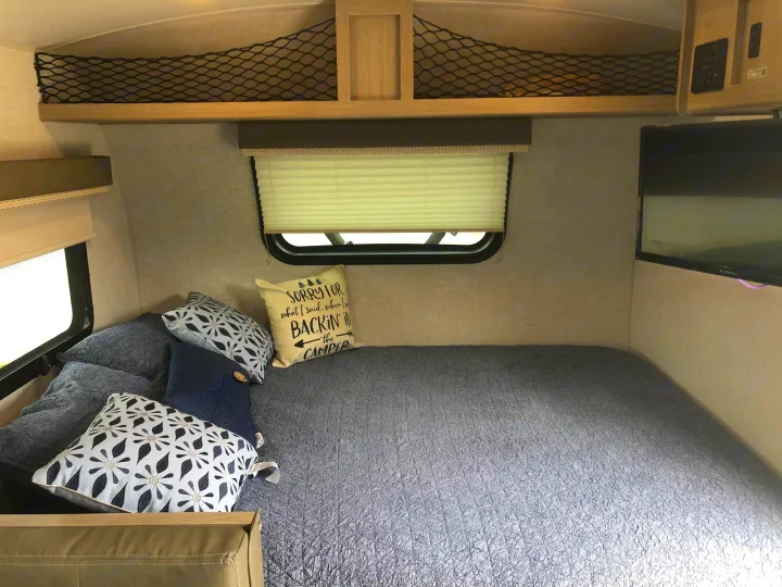 Cozy RV rental interior with a comfy bed, window, TV, and overhead net storage. Ideal for road trips!. Forest River Rockwood Geo Pro 2021