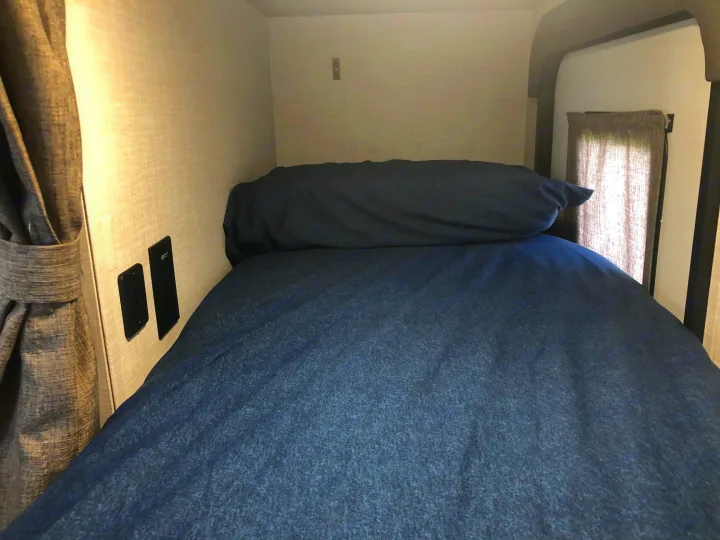 A cozy blue bunk bed in an RV rental, with a tied-back curtain and outlets. A compact sleeping space for travel.. Forest River Rockwood Geo Pro 2021