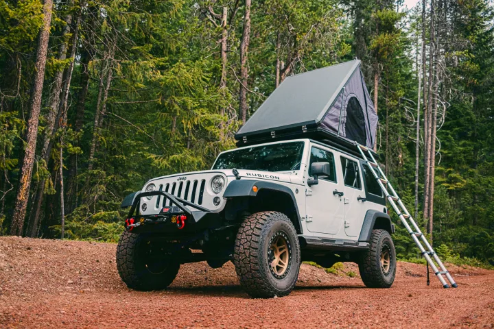 White Jeep Rubicon with rooftop tent on a forest road. An ideal RV rental for off-road camping adventures.. Jeep Wrangler Rubicon 2017