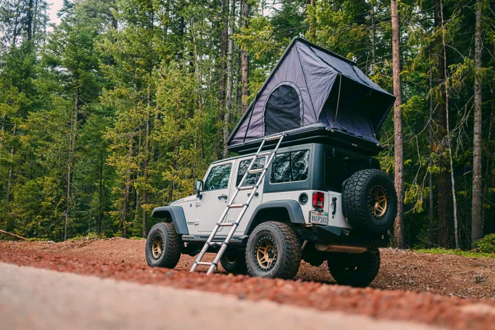 This Jeep with rooftop tent offers a unique RV rental for off-road camping in a lush forest setting.. Jeep Wrangler Rubicon 2017