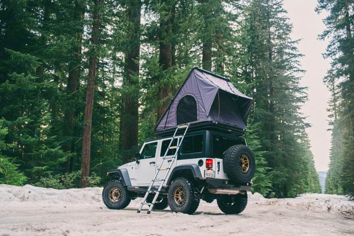 White Jeep with deployed rooftop tent on a snowy forest road. An ideal RV rental for off-road camping adventures.. Jeep Wrangler Rubicon 2017