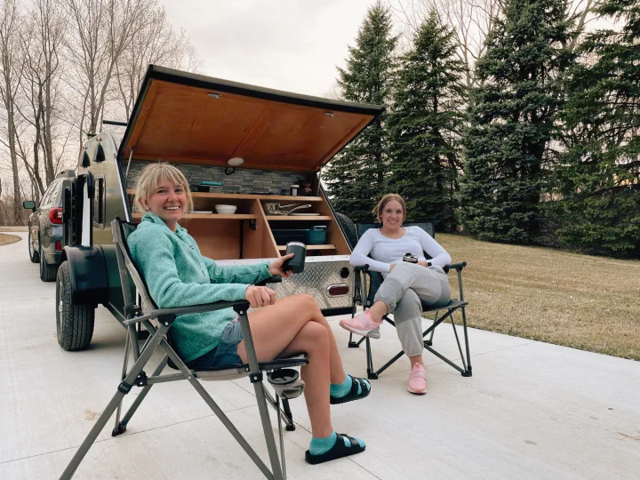 Two women relax by their RV rental, a teardrop camper with an outdoor kitchen. Ideal for easy outdoor living.. American Teardrop Travel Trailer 2016