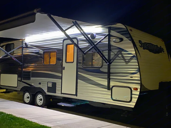 A modern travel trailer, brightly lit with its awning extended, parked at night. Consider an rv rental for your next adventure!. Keystone Springdale 2016