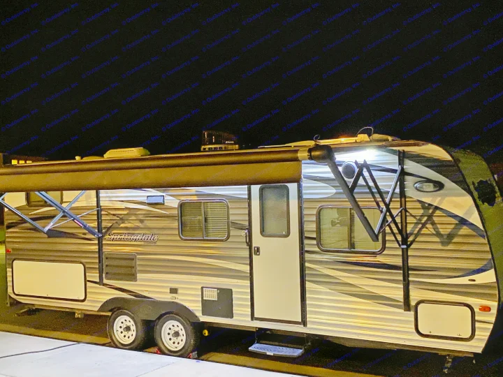 This Springdale travel trailer, an excellent RV rental option, is set up for night use with its awning extended and lights on.. Keystone Springdale 2016