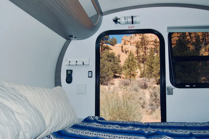 Experience a comfortable RV rental. Inside, a bed, fire extinguisher, and controls. Outside, a stunning desert landscape through the open door.. Bean Bean Stock 2021