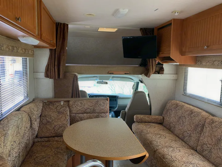Inviting RV rental interior: cozy dinette, patterned sofa, and overhead bunk area with TV, ideal for your next road trip.. Winnebago Access 2007