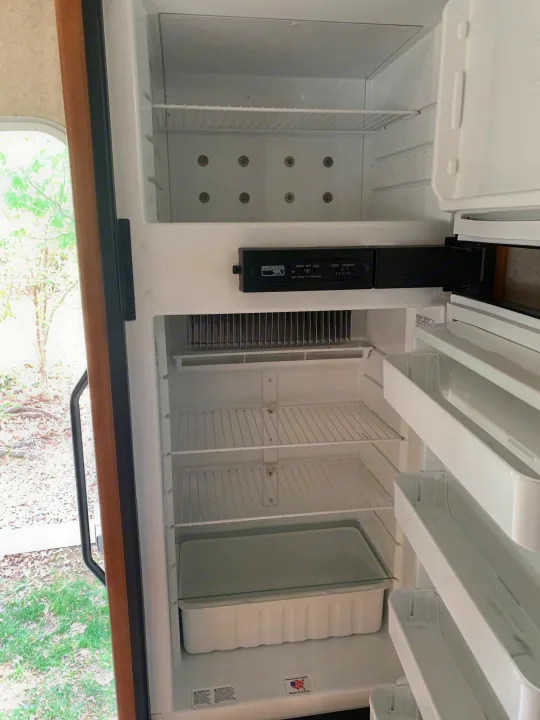 Empty Norcold refrigerator in an rv rental, with open door revealing wire shelves, crisper, and door bins, ready for use.. Winnebago Access 2007