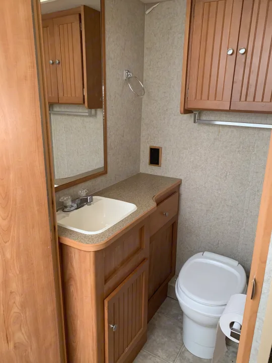 Clean and functional RV rental bathroom featuring a sink, toilet, mirror, and wooden cabinets.. Winnebago Access 2007