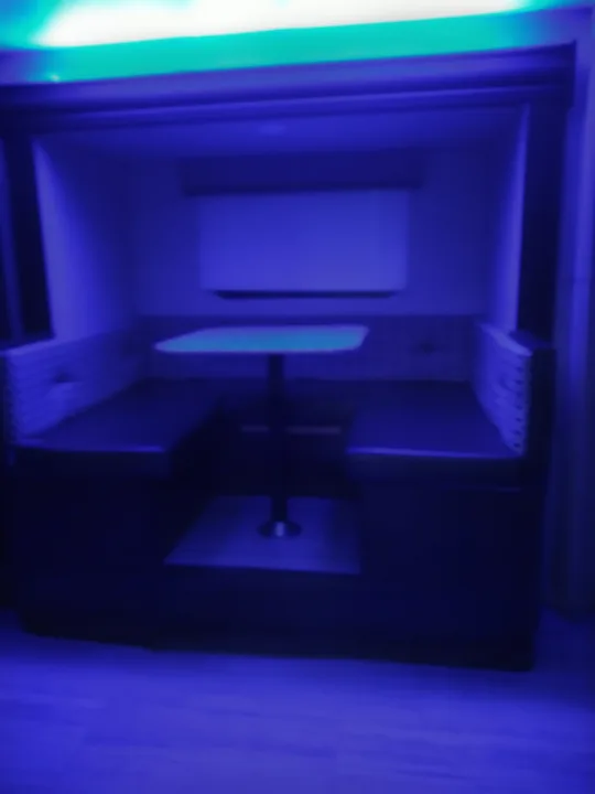 Cozy, blue-lit RV rental interior featuring a compact dining booth with built-in seating and a central table.. KZ Other 2017