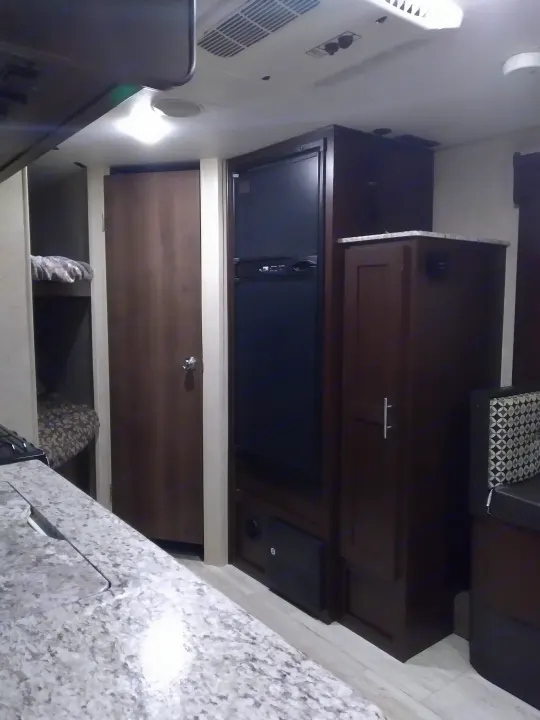 Inside an rv rental: kitchen counter, fridge, bunk beds, and AC unit. Features light floor and dark wood cabinetry.. KZ Other 2017