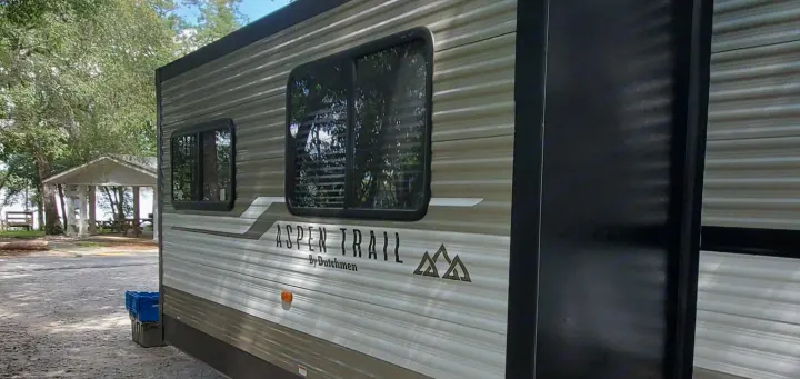Aspen Trail RV rental at a serene campsite with a visible picnic shelter and trees.. Dutchmen Aspen Trail 26BH 2021