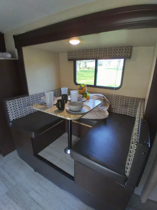Cozy RV rental dinette with patterned bench seating, a table set with dishes, and a window view to nature.. KZ Other 2017