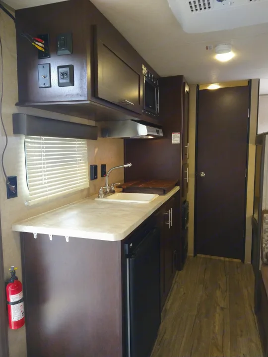 RV rental interior: a compact kitchen area with microwave, sink, and covered stove, designed for efficient mobile living.. Forest River Cherokee Wolf Pup 2017