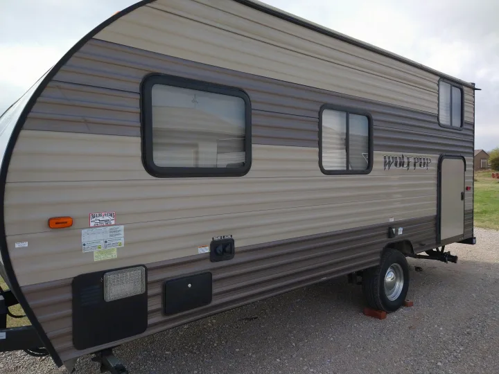 Side view of a brown and beige Wolf Pup travel trailer, a great option for an rv rental, parked on gravel.. Forest River Cherokee Wolf Pup 2017