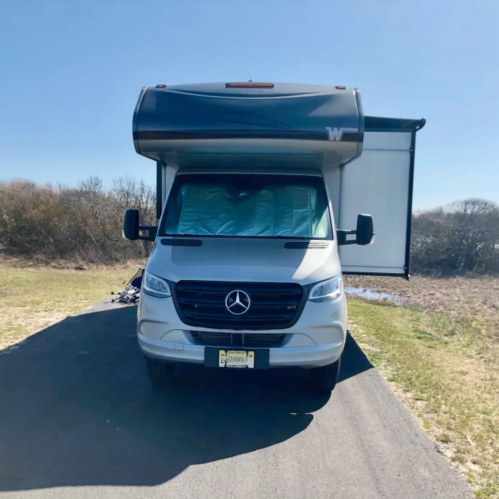 Silver Mercedes-Benz RV rental with sunshade & extended slide-out, on asphalt in dry, grassy landscape.. Winnebago Mercedes Sprinter 2020