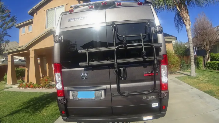 Rear view of a gray Ram ProMaster RV with a Thule bike rack, perfect for your next rv rental adventure.. Thor Sequence 2021