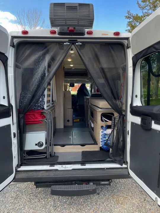 Explore a comfortable RV rental: rear view of a camper van's organized interior with open doors, mesh screen, living space & storage.. Winnebago SOLIS 59 PX Winnebago Camper 2021