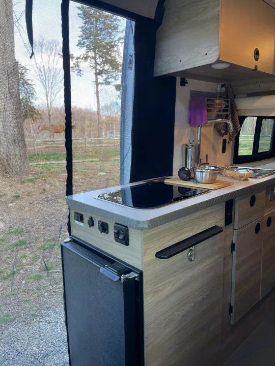 Experience an RV rental: a compact kitchen area with sink, stove, and fridge, plus a serene view of nature including a distant horse.. Winnebago SOLIS 59 PX Winnebago Camper 2021
