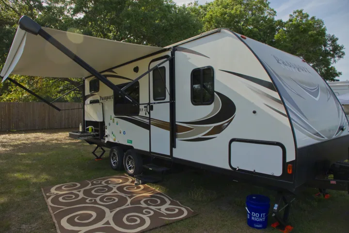An RV rental is fully set up at a grassy campsite with its awning extended and a decorative rug for outdoor living.. Other Passport 2019