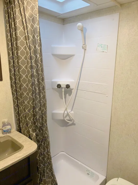 Inside an RV rental: compact bathroom featuring a white shower stall with controls, showerhead, and a stylish gray patterned curtain.. Starcraft Launch 2018