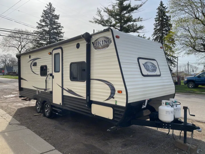 Explore the outdoors with this Viking travel trailer RV rental, showcasing its side door, awning, and front propane tanks.. Viking 21BH 2018