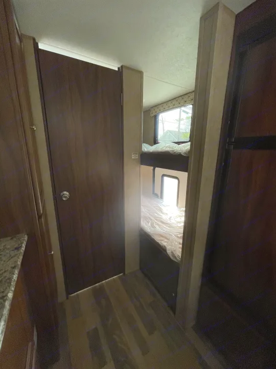 Inside this RV rental, a narrow hallway with a closed door leads to bunk beds, featuring plastic-covered mattresses and a window.. Viking 21BH 2018