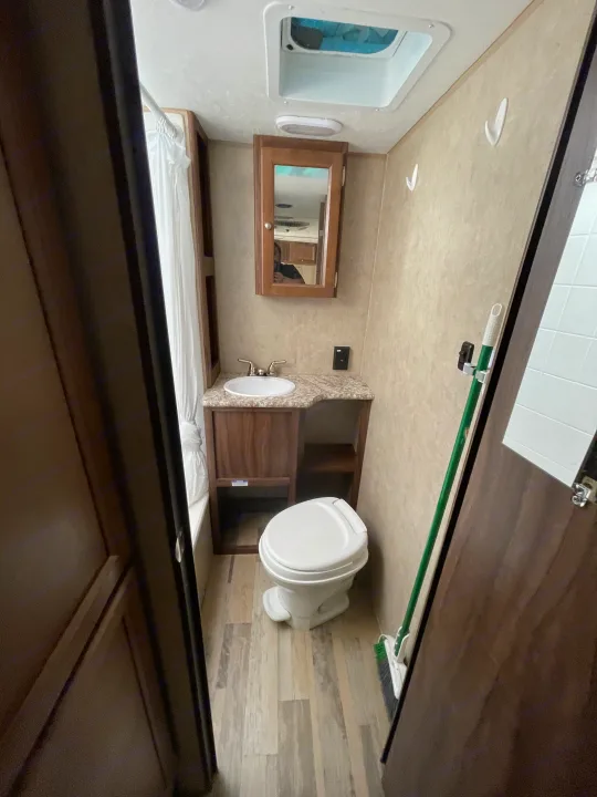 Compact RV rental bathroom features toilet, sink, mirror, shower, and ceiling vent with light.. Viking 21BH 2018