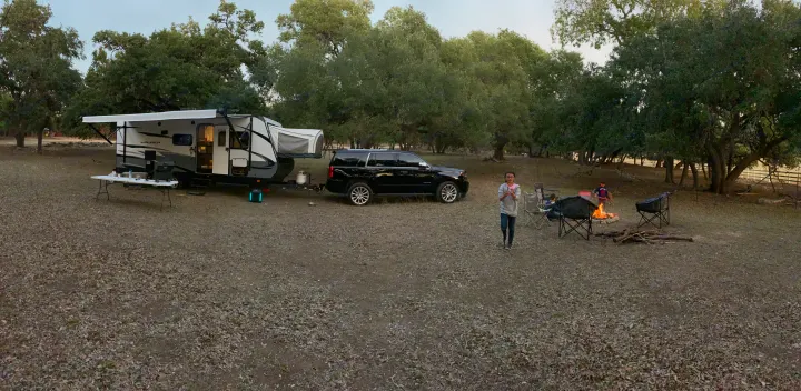 Enjoying an RV rental adventure! A spacious travel trailer, SUV, and cozy campfire highlight this outdoor camping scene with people.. Starcraft Launch 2018