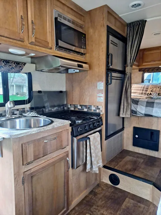 Explore this RV rental's cozy interior, showcasing a well-equipped kitchen with stove, microwave, sink, and wood cabinetry.. Gulf Stream Conquest 2018