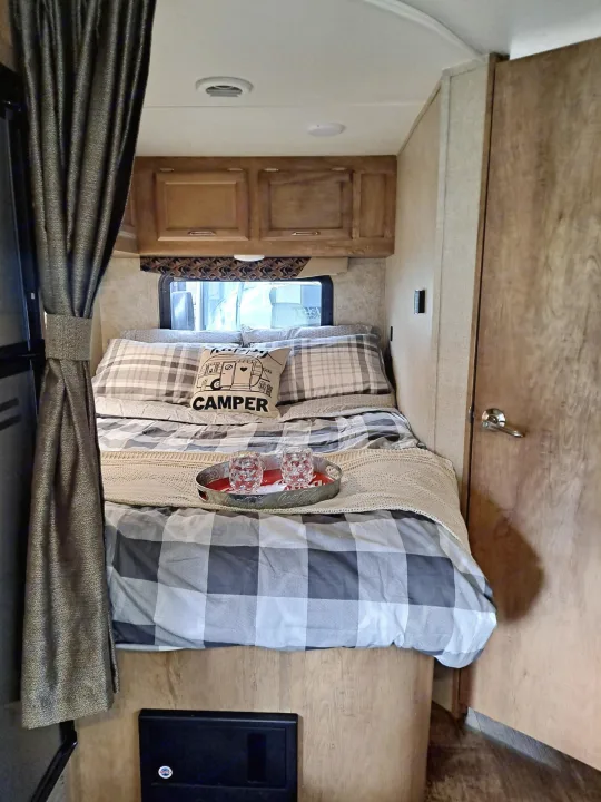 Overhead view of an RV rental sleeping area featuring plaid bedding, "CAMPER" pillow, and a wall-mounted TV.. Gulf Stream Conquest 2018