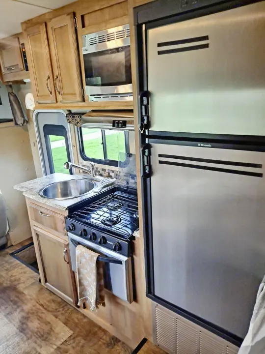 Explore this rv rental's interior! Full kitchen with Dometic fridge, microwave, sink, stove, and wood cabinets.. Gulf Stream Conquest 2018