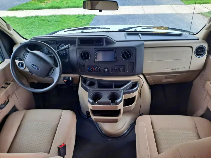 Spacious RV rental interior: driver's view of dashboard, steering wheel, seats, and central console with cup holders.. Gulf Stream Conquest 2018