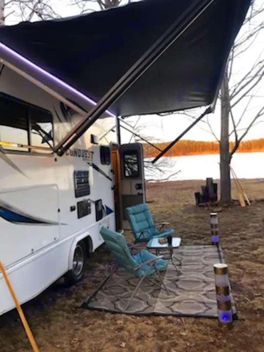 Perfect RV rental camping spot by the water. Awning, outdoor rug, and chairs create a cozy patio setup.. Gulf Stream Conquest 2018