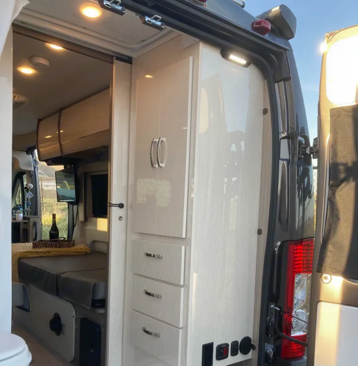 Open doors reveal a modern RV rental interior with bed, storage cabinets, and ambient lighting for comfortable journeys.. Jayco Swift 2021