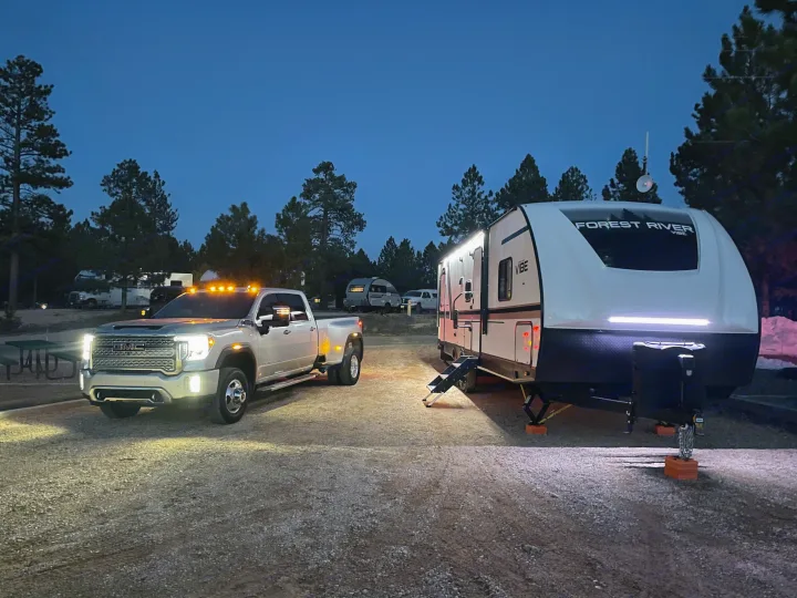 Bright GMC truck & Forest River RV illuminated at a gravel campsite at dusk. Perfect for an rv rental adventure.. Forest River Vibe 2021